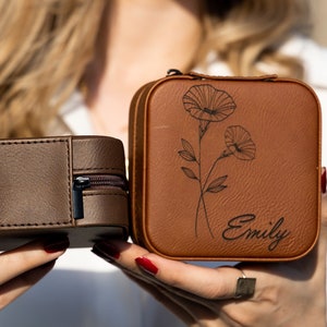 May include: Two brown leather jewellery boxes with zipper closures. One box has a floral design and the name "Emily" engraved on the front. The other box has a plain front.