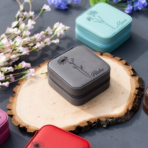 May include: Six small, square, personalised jewellery boxes with floral designs. The boxes are in various colours, including pink, blue, grey, brown, and black. Each box has a different name engraved on it: Rebecca, Maria, Alisha, and three others.