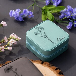 May include: A teal blue jewellery box with a zipper closure. The box has a floral design and the name "Marie" engraved on the front.