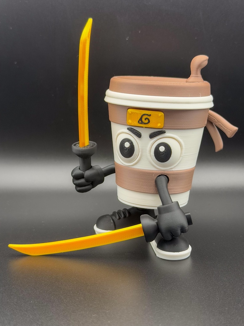 May include: A 3D-printed coffee cup figure with a cartoonish design, holding two yellow swords. The cup has a brown lid, a white body with a brown band, and black gloves and shoes. A yellow emblem is on the cup.