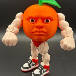 May include: A whimsical orange-shaped figurine with a human face, green leaf, and muscular arms and legs. The figurine is wearing red shorts and black, white, and red sneakers. The figure is a unique and humorous decorative item.