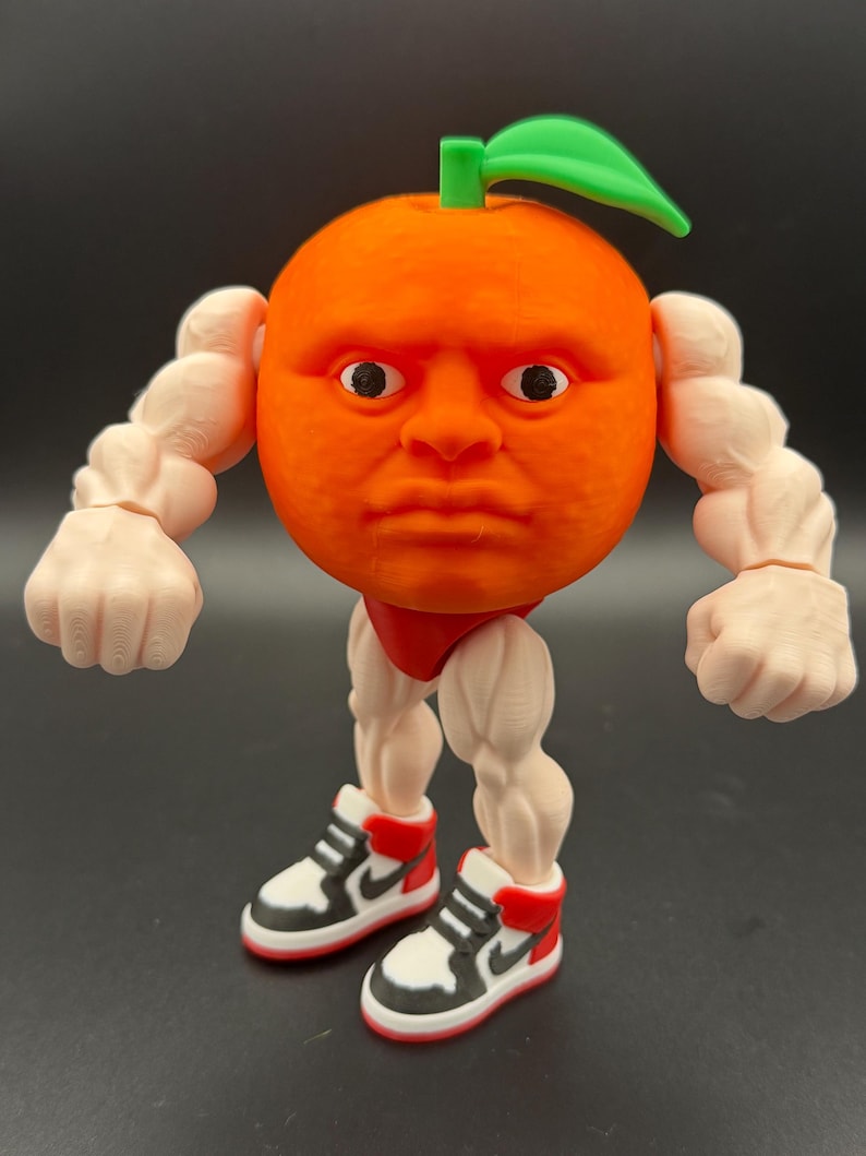 May include: A whimsical orange-shaped figurine with a human face, green leaf, and muscular arms and legs. The figurine is wearing red shorts and black, white, and red sneakers. The figure is a unique and humorous decorative item.