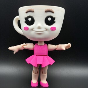 May include: A whimsical white teacup doll with a smiling face, brown eyebrows, and black eyes. The doll wears a pink dress and ballet shoes, with articulated arms and legs. The doll is a unique decorative item.