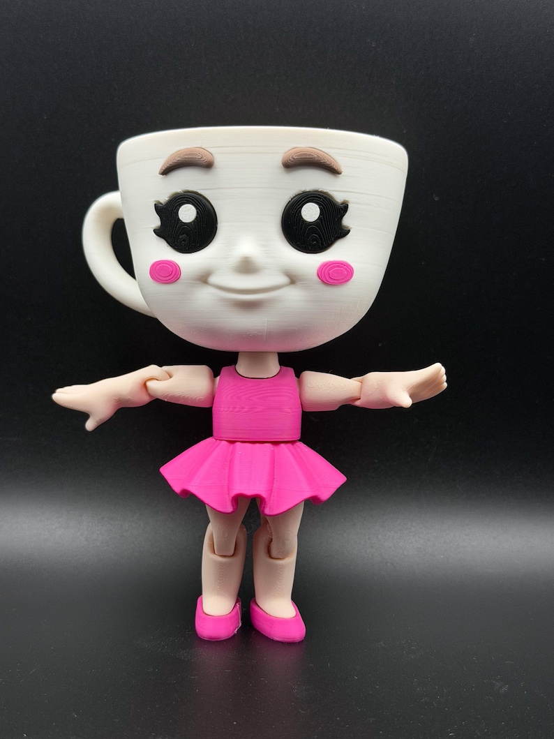 May include: A whimsical white teacup doll with a smiling face, brown eyebrows, and black eyes. The doll wears a pink dress and ballet shoes, with articulated arms and legs. The doll is a unique decorative item.