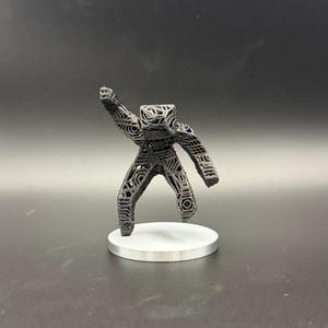 May include: A dark grey, 3D-printed figurine of a person with an arm raised. The figure has a geometric, open design and stands on a small, white circular base. The background is a solid, dark grey.
