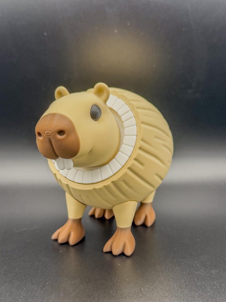 May include: A tan-colored capybara figurine with a detailed textured body, brown nose, and white teeth. The figurine has a white collar and small, dark eyes. The capybara is standing on four brown feet.