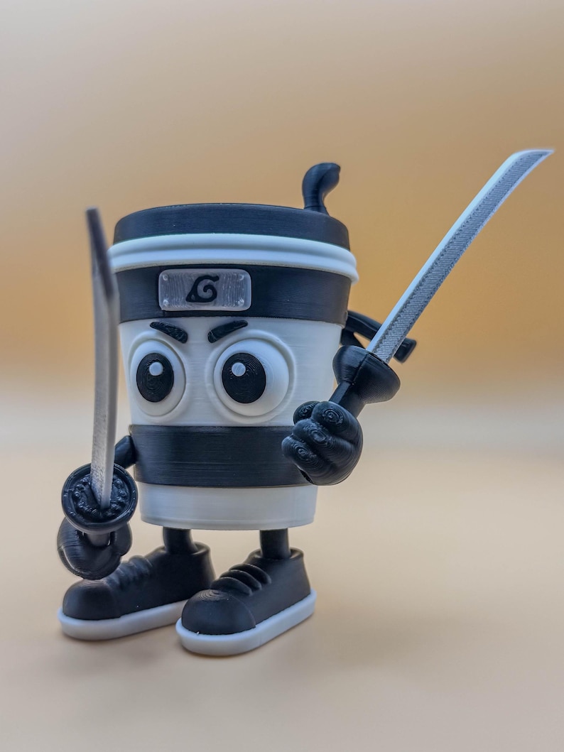 May include: A 3D-printed coffee cup character with large eyes, a black and white color scheme, and a ninja headband. The cup is holding two toy swords and wearing black sneakers. A silver emblem with a swirl is on the cup.