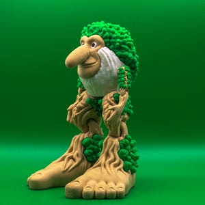 May include: A quirky figurine of a forest creature with a large nose, green leafy hair, and tree-like legs and feet. The figure has a tan face and body, with green accents. The background is a solid green.