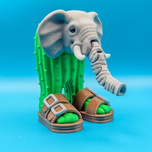 May include: A whimsical 3D-printed sculpture featuring a gray elephant head atop a green cactus body. The elephant wears brown sandals with green footbeds. The sculpture is set against a bright blue background.