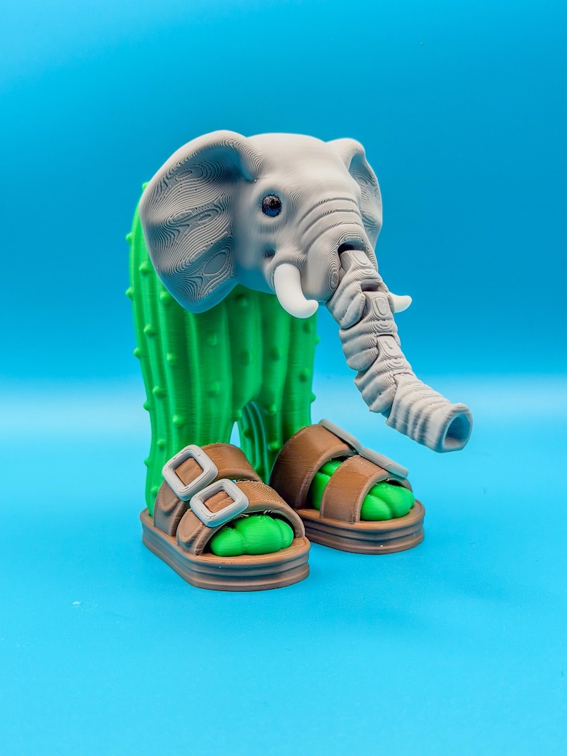 May include: A whimsical 3D-printed sculpture featuring a gray elephant head atop a green cactus body. The elephant wears brown sandals with green footbeds. The sculpture is set against a bright blue background.