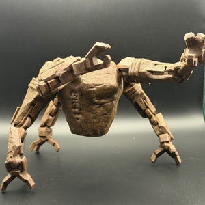 Könnte beinhalten: Eine braune, bewegliche Roboterfigur mit strukturierter Oberfläche. Der Roboter hat einen humanoiden Torso, vier Beine und zwei Arme, alle mit gelenkigen Segmenten. Die Arme sind erhoben und die Beine gespreizt. Die Figur besteht aus einem festen Material.