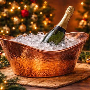 May include: A copper-colored champagne bucket filled with ice holds a green bottle of champagne. A champagne flute is next to the bucket. The background features a Christmas tree with lights and ornaments. Festive holiday theme.