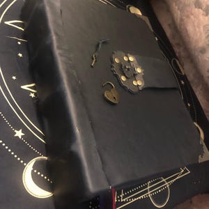 May include: A black leather-bound journal with a heart-shaped padlock and key. The journal has a decorative metal clasp with gold accents.