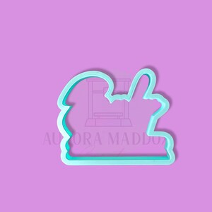 May include: A light blue plastic cookie cutter shaped like a hand giving a thumbs up. The cookie cutter is on a light purple background.
