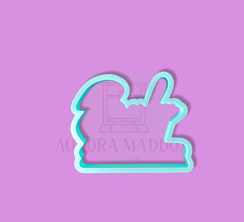 May include: A light blue plastic cookie cutter shaped like a hand giving a thumbs up. The cookie cutter is on a light purple background.