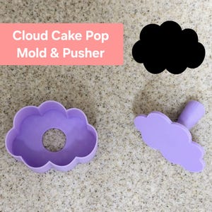 May include: Purple plastic cloud cake pop mold and pusher. The mold is shaped like a cloud with a hole in the center. The pusher is also shaped like a cloud and has a handle.