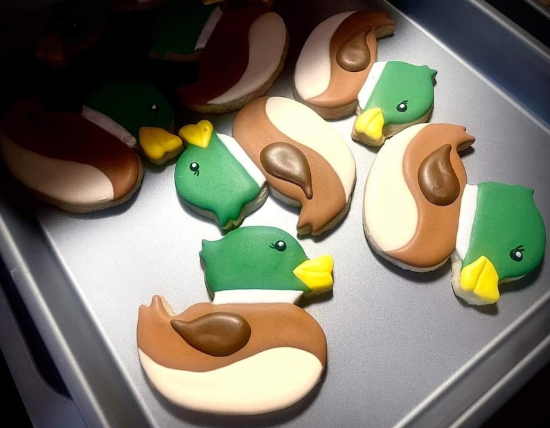 May include: A collection of decorated sugar cookies shaped like ducks. The cookies are brown, green, and yellow with white icing.