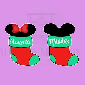 Op de afbeelding: Twee rode en groene kerstsokken met Mickey Mouse oren. De sok links heeft de naam "Aurora" erop geschreven. De sok rechts heeft de naam "Maddox" erop geschreven.