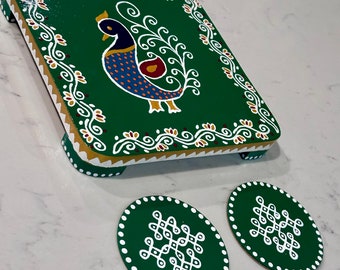 May include: A green square wooden tray with a peacock design painted on it. The tray has a white border and gold accents. There are two smaller green coasters with white designs.