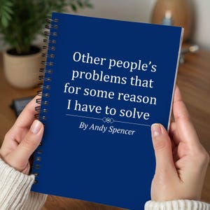 May include: A dark blue spiral-bound notebook with the text "Other people's problems that for some reason I have to solve" by Andy Spencer. The notebook is held open, revealing the white pages.