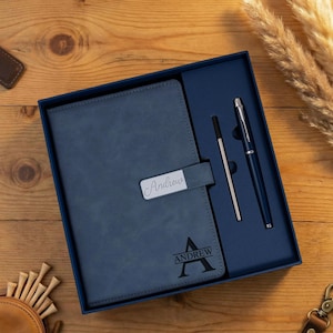 May include: A blue leather journal and pen set in a navy blue gift box. The journal has the name "Andrew" engraved on a silver plate and the name and initial on the front. A silver pen and a pen refill are included.