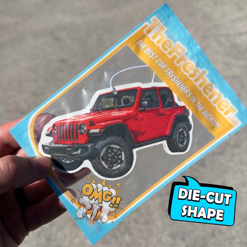 Pu&ograve; includere: Un profumatore per auto rosso a forma di Jeep Wrangler in una busta di plastica trasparente con bordo blu e giallo. La busta ha il testo "The Freshener.com" e "The Best Car Fresheners in the World!" stampato su di essa. Il profumatore &egrave; tagliato a forma di Jeep Wrangler.