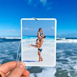 K&ouml;nnte beinhalten: Ein Paar am Strand, der Mann h&auml;lt die Frau in seinen Armen. Beide l&auml;cheln und schauen sich an. Der Strand ist wei&szlig;er Sand und das Wasser ist blau.