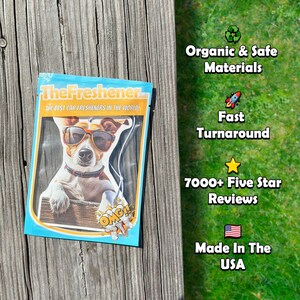 K&ouml;nnte beinhalten: Eine wei&szlig;e Verpackung mit blauem Rand, auf der ein Cartoon-Hund mit Sonnenbrille und rotem Halsband zu sehen ist. Die Verpackung tr&auml;gt den Schriftzug "TheFreshener.com" und "The best car fresheners in the world!" Die Verpackung liegt auf einer Holzoberfl&auml;che.