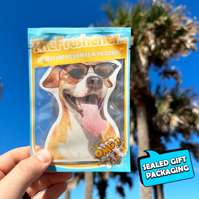 Puede incluir: Un paquete sellado de un ambientador de coche con un perro que lleva gafas de sol. El paquete es azul y amarillo con el texto "TheFresher.com" y "The best car fresheners in the world!" El paquete tambi&eacute;n tiene el texto "OMG!" y "Sealed Gift Packaging".