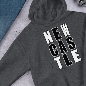 Op de afbeelding: Een donkergrijs hoodie met het woord "NEWCASTLE" in witte letters op de voorkant.