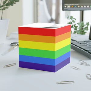 May include: A rainbow-colored stack of sticky notes with a white top sheet. The notes are arranged in the order of the rainbow, with red at the top and purple at the bottom.