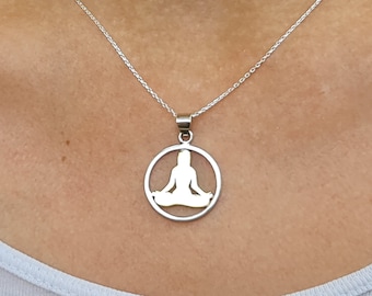 May include: A silver chain necklace with a pendant featuring a gold silhouette of a person sitting in a yoga pose inside a circle.