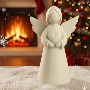 May include: A cream-coloured angel figurine holding a heart, with outstretched wings. The angel is set against a backdrop of a fireplace and a Christmas tree, creating a festive holiday scene. The figurine is a decorative item.