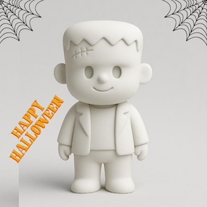 May include: A white, cartoon-style Frankenstein's monster figurine with stitched details on the head. The figure is wearing a jacket and has a smiling face. The words "HAPPY HALLOWEEN" are printed in orange. Spiderwebs are in the background.