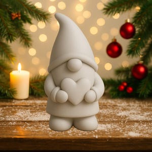 May include: A white gnome figurine holding a heart, set against a festive backdrop with Christmas ornaments and a lit candle. The gnome has a large nose and a pointed hat, perfect for holiday decor.
