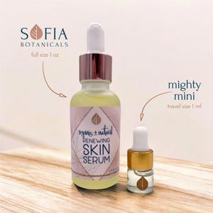 Op de afbeelding: Twee glazen flessen Sofia Botanicals Renewing Skin Serum. De fles van volledige grootte is 29,57 ml en de reisgrootte is 1 ml. Beide flessen hebben een druppelaar en een roze en wit etiket met de tekst "organic + natural" en "Renewing Skin Serum."