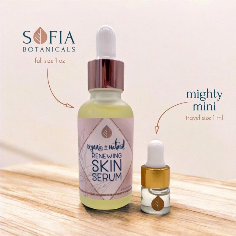 Op de afbeelding: Twee glazen flessen Sofia Botanicals Renewing Skin Serum. De fles van volledige grootte is 29,57 ml en de reisgrootte is 1 ml. Beide flessen hebben een druppelaar en een roze en wit etiket met de tekst "organic + natural" en "Renewing Skin Serum."