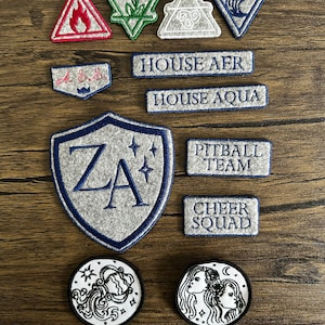 May include: A collection of embroidered patches in various shapes and designs. Includes triangular patches with flame and leaf motifs, rectangular patches with text, and circular patches with illustrations. The patches are in shades of red, green, blue, and gray.