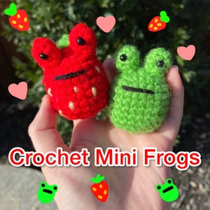 May include: Two crocheted mini frogs, one red and one green, are held in a hand. The red frog is shaped like a strawberry and the green frog has a simple design. The text "Crochet Mini Frogs" is at the bottom of the image.