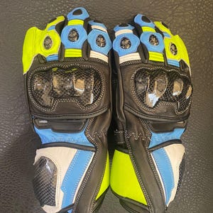 May include: A pair of black leather motorcycle gloves with blue and neon green accents. The gloves feature carbon fibre knuckle protection and padding on the palm and fingers.