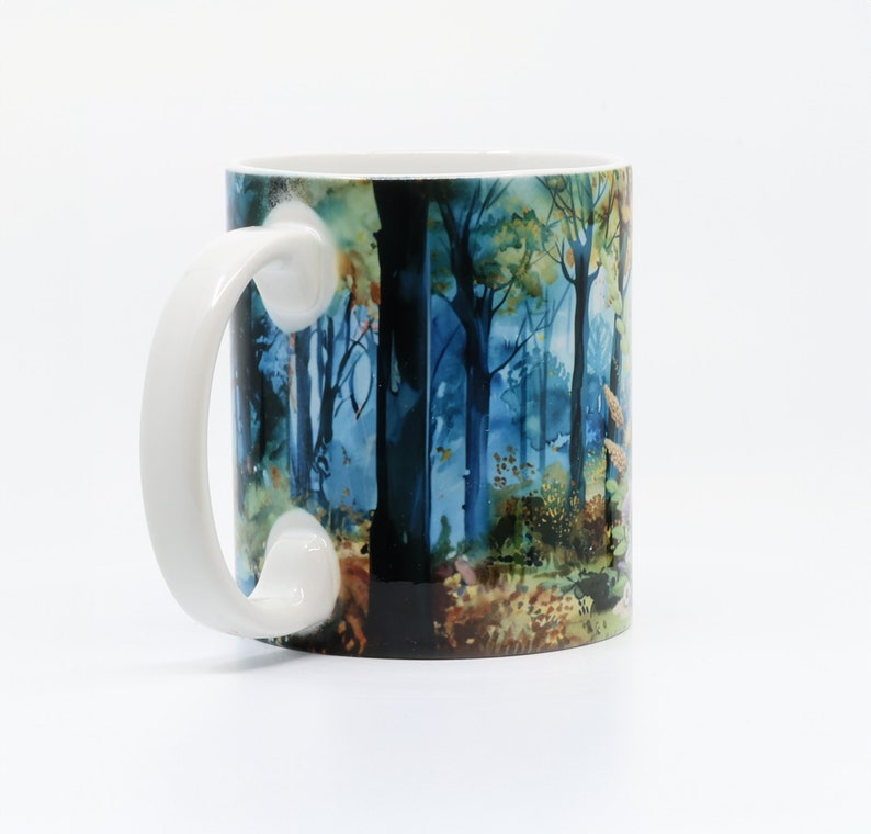 May include: White ceramic mug with a blue and green watercolor design of a forest scene. The mug has a large handle.