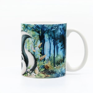 May include: White ceramic mug with a colorful illustration of a skunk in a forest setting. The skunk is black and white with a white stripe down its back. The forest is a watercolor style with blue, green, and brown colors.