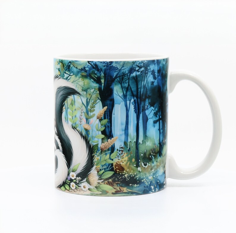 May include: White ceramic mug with a colorful illustration of a skunk in a forest setting. The skunk is black and white with a white stripe down its back. The forest is a watercolor style with blue, green, and brown colors.