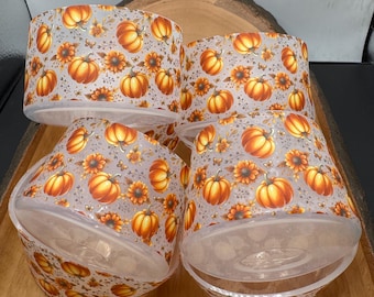 May include: Four clear, cylindrical containers with a fall-themed design. The containers are decorated with orange pumpkins and yellow sunflowers on a light gray background. The containers are arranged on a wooden tray.