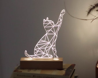 May include: A white geometric cat-shaped night light on a wooden base. The light is on and illuminating the cat shape.