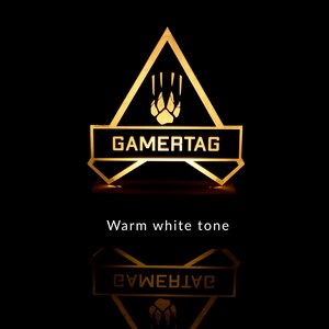 May include: A black and gold gamertag sign with a paw print and the word "GAMERTAG" in white letters. The sign is illuminated with a warm white light.