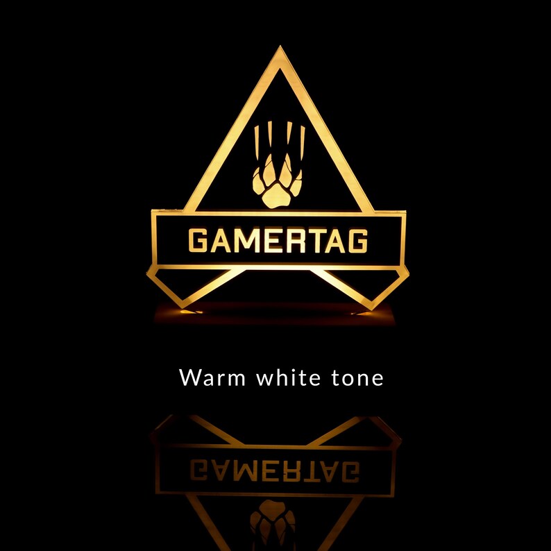 May include: A black and gold gamertag sign with a paw print and the word "GAMERTAG" in white letters. The sign is illuminated with a warm white light.