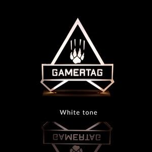 May include: A white illuminated sign with a black triangle shape and the word "GAMERTAG" in white letters. The triangle has a white paw print inside. The sign is on a black background.