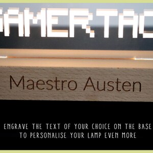 May include: A wooden base with the text "GAMERTAG" engraved on it. The base is illuminated by a clear acrylic sign with the text "GAMERTAG" in white pixelated letters. The base also has the text "Maestro Austen" engraved on it.