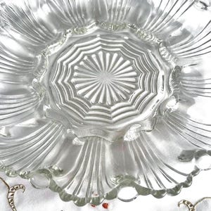 Pode incluir: Prato de servir de vidro transparente com borda ondulada e design radial texturizado no centro. O prato tem uma borda canelada em forma de pétala, provavelmente para servir aperitivos ou sobremesas.